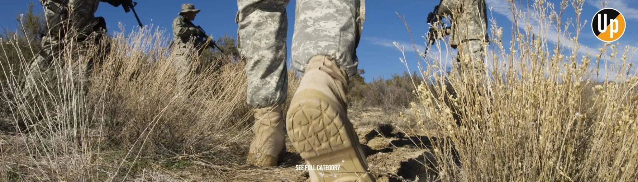 slider-tactical-1.webp Στρατιώτες με στολή παραλλαγής βαδίζουν σε ξηρό τοπίο με θάμνους, προβάλλοντας ανθεκτικά στρατιωτικά υποδήματα και κάλτσες Uphill